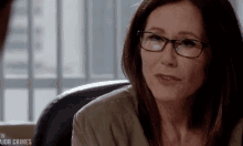 a woman wearing glasses is sitting in front of a sign that says " major crimes "