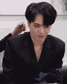 a man in a suit is sitting at a table while another man holds his hair .
