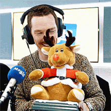 a man wearing headphones holds a stuffed reindeer in front of a microphone that says magie