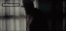 a man in a cowboy hat is standing in front of a window with the website kulfyapp.com in the corner .