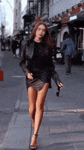 a woman in a black leather skirt and jacket is walking down a street .