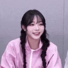 a girl with braids is wearing a pink jacket and smiling at the camera .