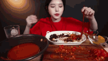 a woman in a red shirt is eating a plate of food with a wooden spoon .
