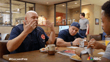 a group of firefighters are sitting at a table in a diner with a chicago fire logo on the table