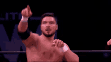 a shirtless wrestler with a beard is standing in a wrestling ring with his arm in the air .