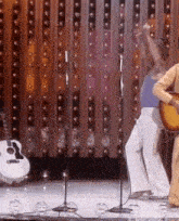 a man is playing a guitar on a stage while another man is dancing .