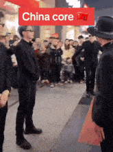 a man in a hat stands in front of a crowd with a red sign that says china core