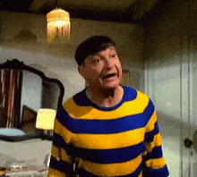 a man wearing a blue and yellow striped sweater is standing in a room