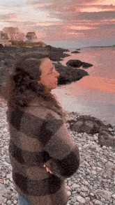 a woman is standing on a rocky beach looking at the ocean .