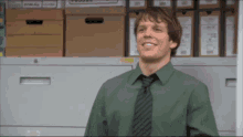 a man in a green shirt and tie is smiling in front of a filing cabinet