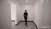 a woman in a black suit is standing in an empty room with the words made in animatica on the bottom