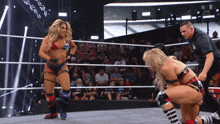 a woman in a bikini is kneeling down in a wrestling ring with a referee