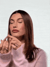 a woman wearing a pink sweater is applying makeup to her lips