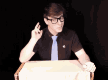a man wearing glasses and a black shirt with a blue tie is sitting at a table