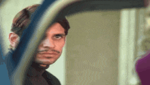 a man with a moustache is looking at himself in a mirror