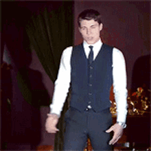 a man in a vest and tie is standing in a dark room