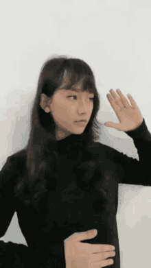 a woman in a black turtleneck is making a gesture with her hand