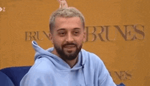 a man with a beard is laughing while wearing a blue hoodie and a crown on his head .