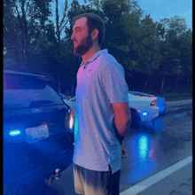 a man in a blue shirt is standing next to a police car .