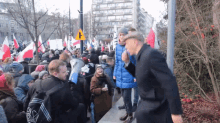 a man in a black coat stands in front of a crowd with flags and a sign that says ' a ' on it