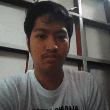 a man wearing a white t-shirt with the word raja on it looks at the camera