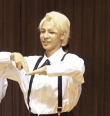a man with blonde hair wearing suspenders and a white shirt smiles