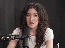 a woman with curly hair stands in front of a microphone with a clock on it that says 1:51