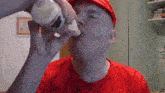a man in a red shirt drinks from a bottle with rad du on the wall behind him