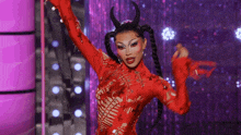 a drag queen in a red costume with horns is dancing on stage .