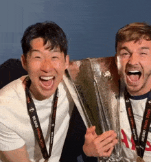 two men holding a trophy with one wearing a lanyard that says ' uefa champions league '