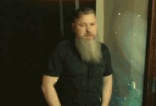 a man with a beard is standing in front of a door with his arms crossed .