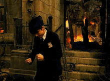 a man in a suit is standing in front of a burning building and a fence .