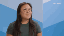 a woman wearing glasses is smiling in front of a blue wall that says elite daily on it