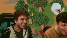 two men are sitting in front of a video game screen and smiling .
