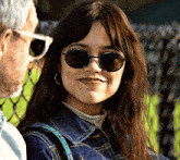 a woman wearing sunglasses and a denim jacket looks at a man