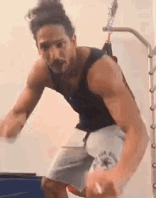 a man in a tank top and shorts is jumping in the air while holding a rope .
