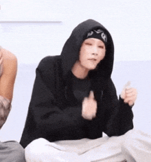 a person wearing a black hoodie and a bandana is sitting on the floor and giving a thumbs up .