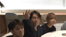 a group of young men are sitting at a table and one of them is waving