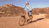 a man in a blue robe is riding a bike on a dirt road .