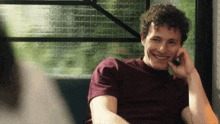 a young man with curly hair is smiling with his hand on his face