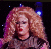 a drag queen with blonde hair and red lips is wearing a black top and a black leather jacket .