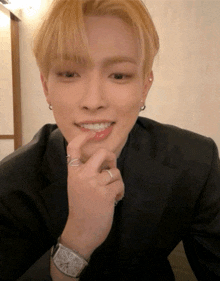 a young man wearing a watch and a ring on his finger looks at the camera