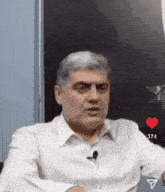 a man in a white shirt with a microphone on his neck is sitting in front of a blackboard