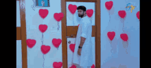 a man in a white shirt is standing in front of a door decorated with red hearts and balloons .