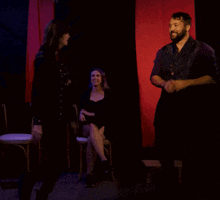 a woman sitting in a chair talking to another woman in a dark room