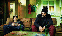 two men are sitting on a couch with a bottle of beer on the table