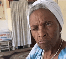 an elderly woman wearing a white headband and pearls is making a funny face .