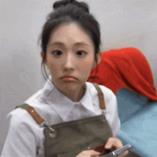 a woman wearing a white shirt and an apron is holding a cell phone .