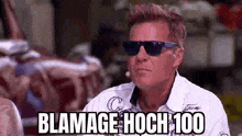 a man wearing sunglasses and a white shirt is standing in front of a microphone and saying blame hoch 100 .