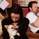 a woman holds a small dog in her arms while a man sits behind her